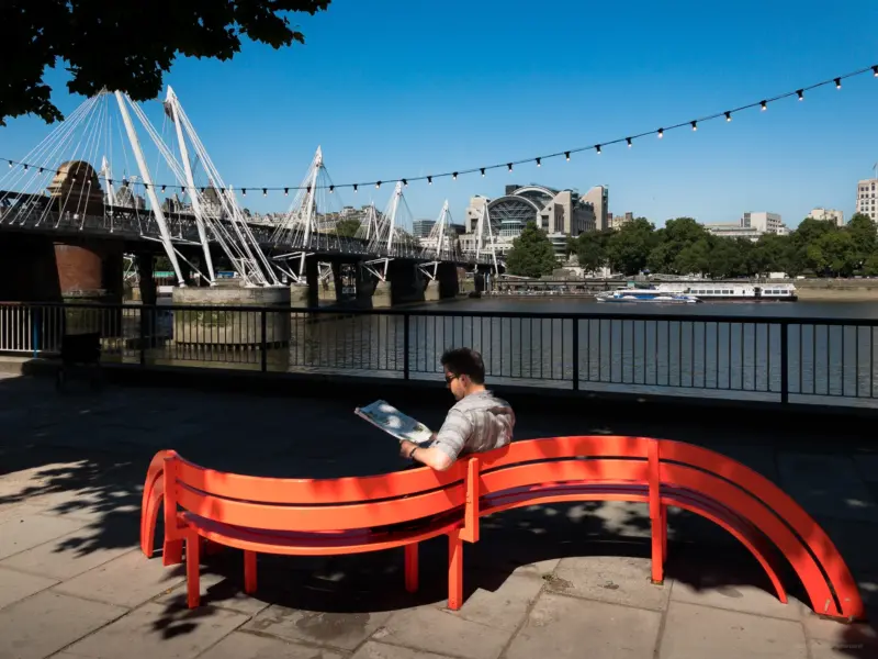 A man reading a newspaper on an orange bench at the bank of the Themes - London, UK - iPhone Photography