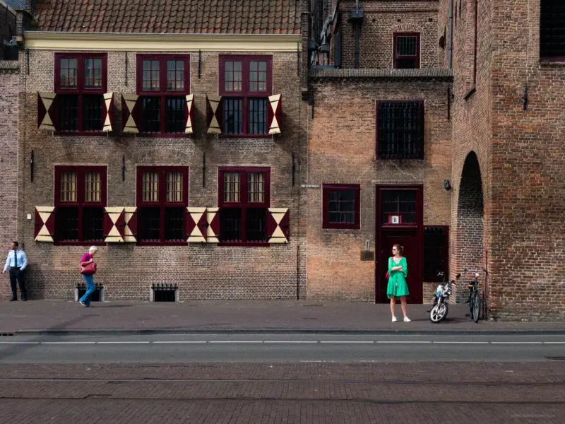 A woman in a green dress in front a maroon door of a brick veneer building - The Hague, Netherlands